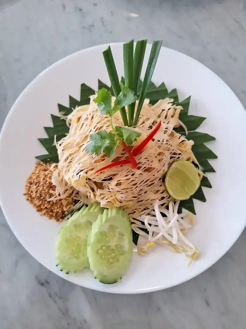 Pad thai on a banana leaf with lime, ground peanuts, bean sprouts and cucumber
