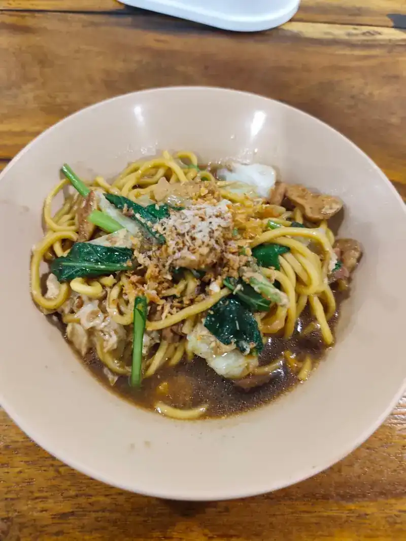 Yellow noodles with greens and fried garlic in a dark sauce