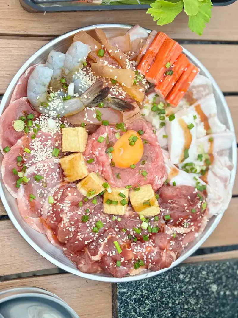 A platter of sliced pork, prawns, crab sticks, tofu and an egg yolk, ready for the grill
