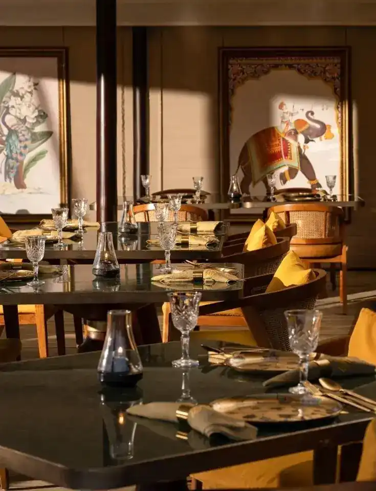 Dark stone tables set with cut glass and brass plates, mustard cushions, an elephant painting on the wall