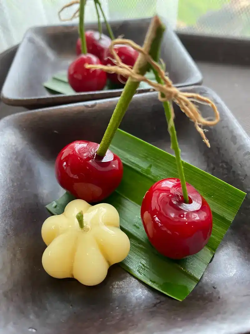 Small Thai sweets shaped like red cherries and a yellow pumpkin, on a banana leaf