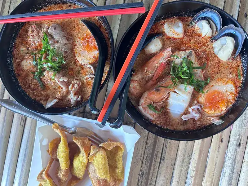 Two bowls of creamy tom yum, one with pork and one with prawns, squid and mussels, beside fried wontons