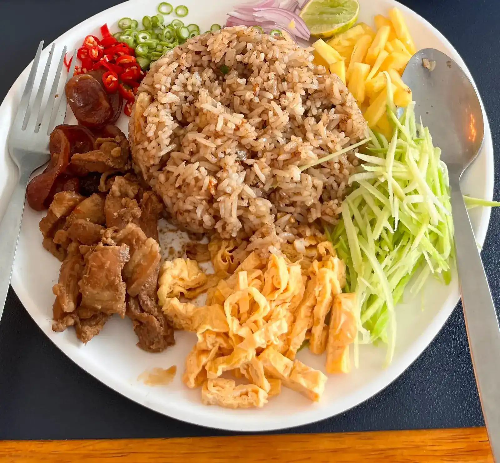 A plate of khao kluk kapi, rice tossed in shrimp paste, with sweet pork, egg, green mango and chillies