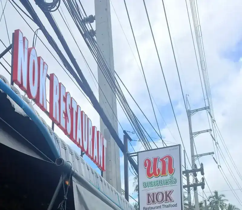 NOK RESTAURANT in red letters above the awning, and the white นก sign on its post