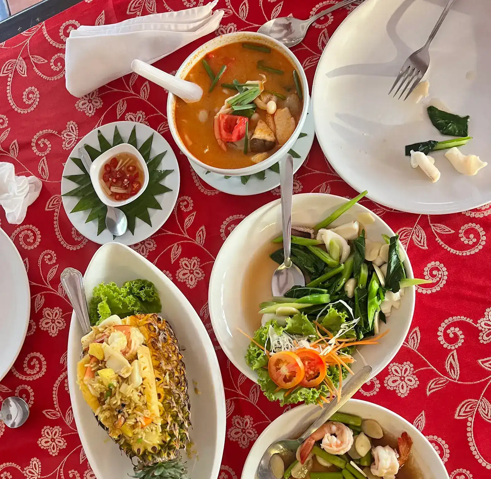 Pineapple fried rice served in the pineapple, a bowl of tom yum and stir-fried greens with seafood, on Tawai's red tablecloth
