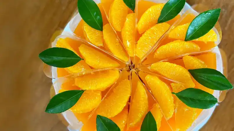 An orange cake cut into slices, each topped with orange segments and green leaves