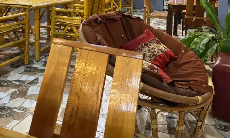 A rattan bowl chair with a red cushion beside bamboo chairs, inside the restaurant at night