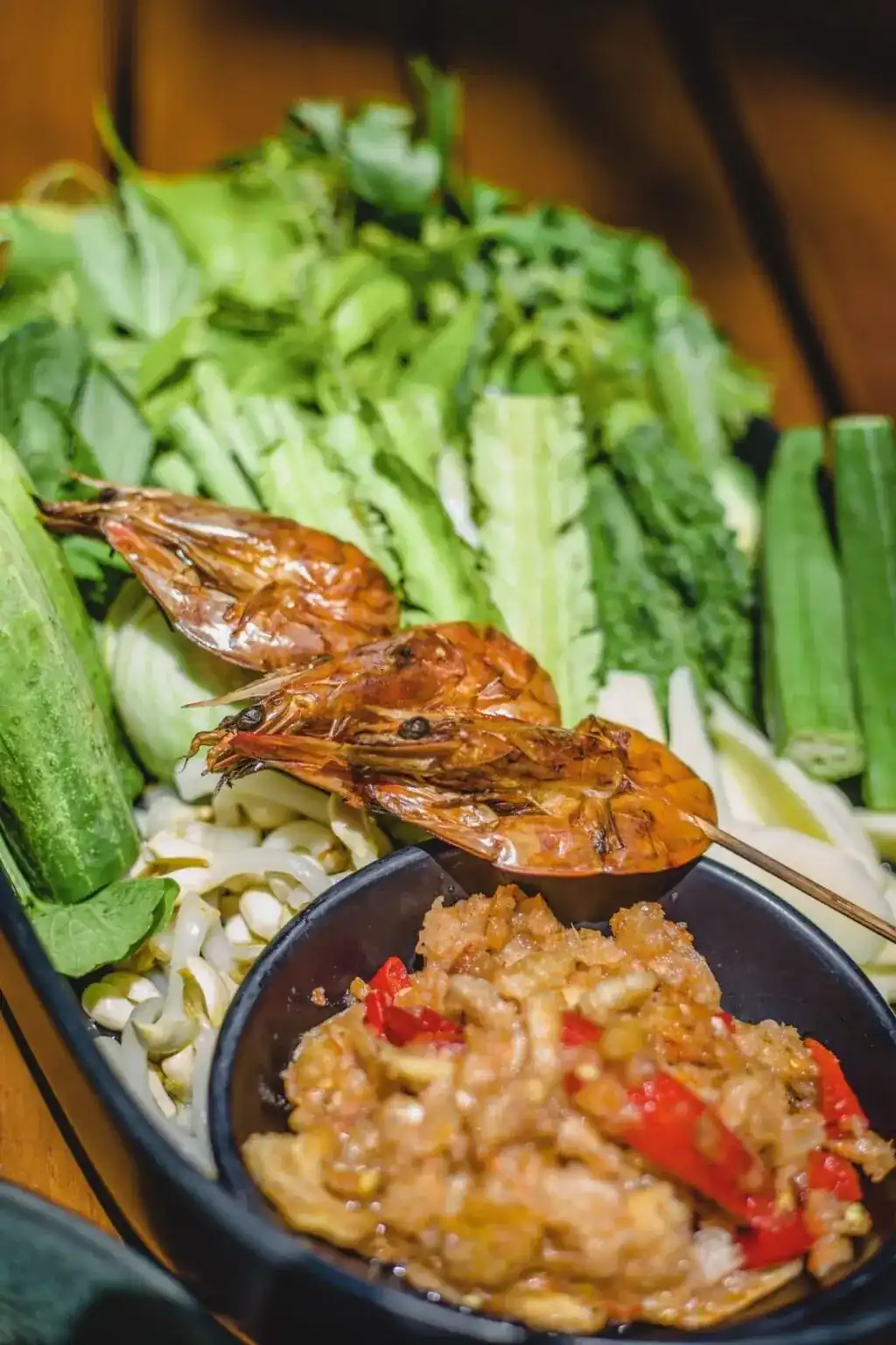 Grilled smoked shrimps on a skewer over a bowl of chili dip, with fresh local vegetables