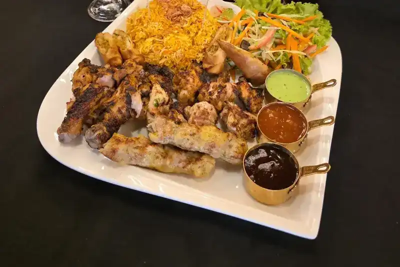 A grill platter of kebabs and grilled chicken with rice, salad and three dipping sauces