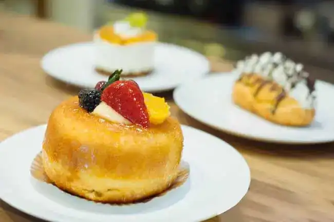 A rum-baba style cake topped with strawberry and blackberry, more pastries behind