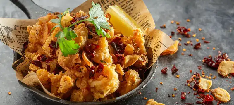 Crisp fried calamari with dried chili and lemon in an iron pan