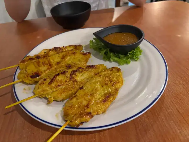 Grilled chicken satay skewers with a bowl of peanut sauce and lettuce