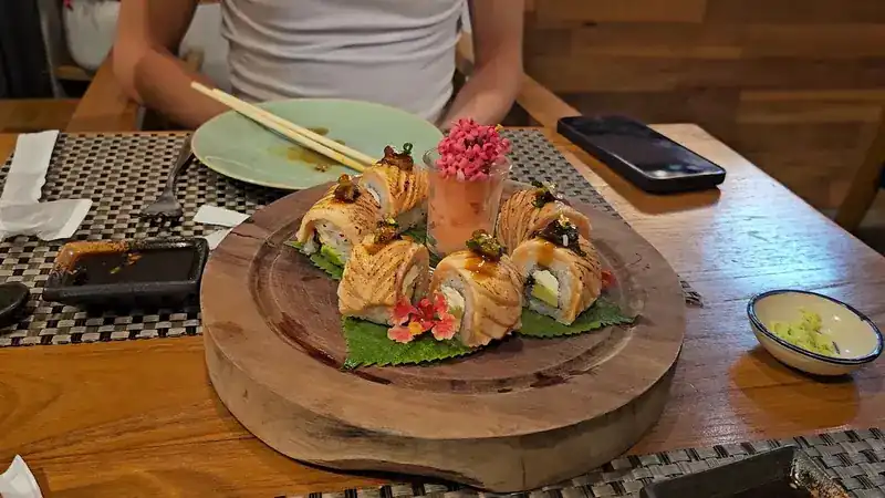 Seared salmon rolls with a pink flower on a round wooden board / โรลแซลมอนเบิร์นหน้าบนเขียงไม้กลม ประดับดอกไม้สีชมพู
