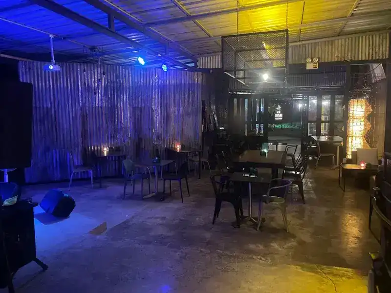 The tin-walled music room under blue stage lights, with speakers, tables and candles