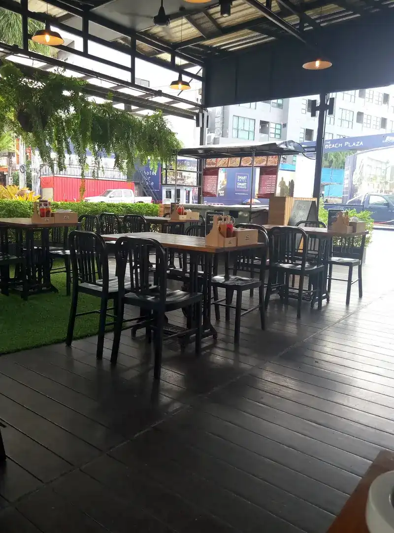 The covered terrace, with dark wooden tables and chairs, a strip of grass and hanging plants