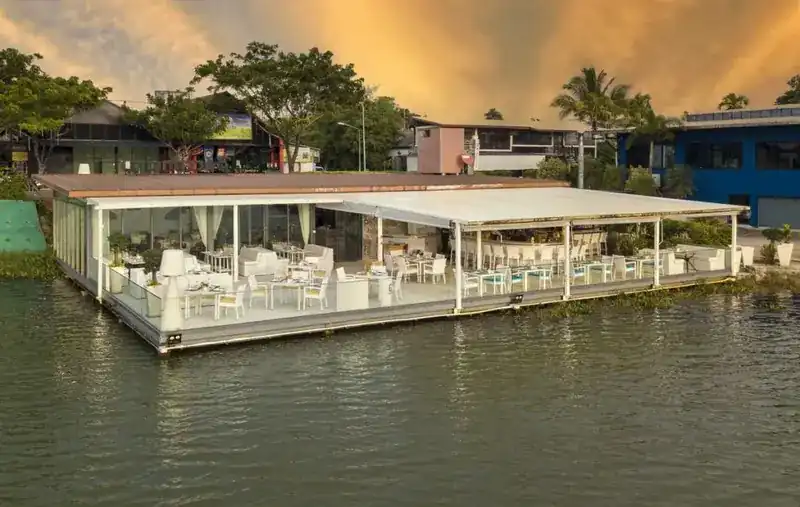 Bocconcino seen from the lake at dusk: a low white pavilion on the water under an amber sky