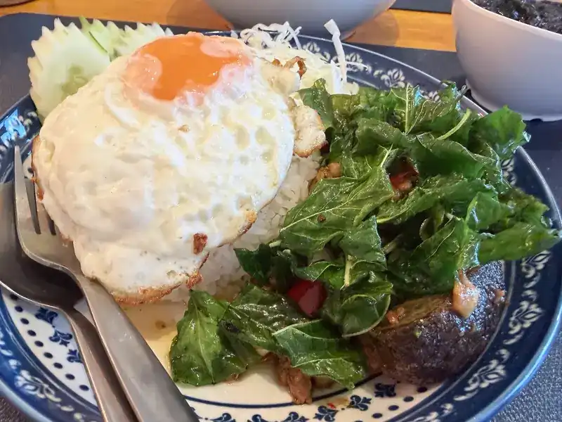 A fried egg over rice with stir-fried greens