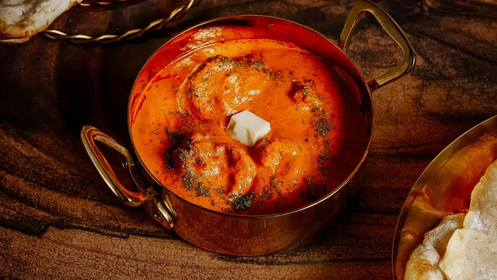 A copper pot of butter chicken with a pat of butter melting on top