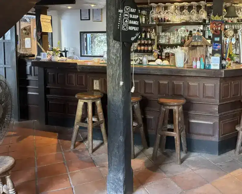 The panelled oak bar with wooden stools on a terracotta floor