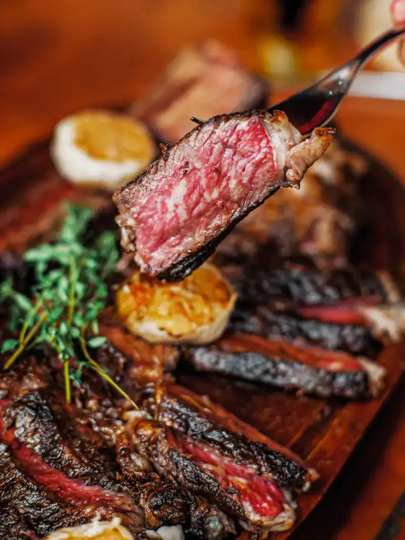 One slice of steak lifted on a fork, pink in the middle and charred at the edge