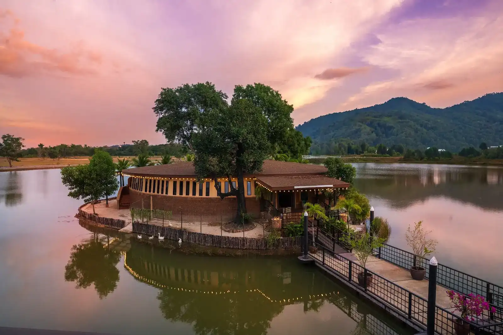 The Ashes island in the lake at dusk, string lights reflected in the water and mountains behind