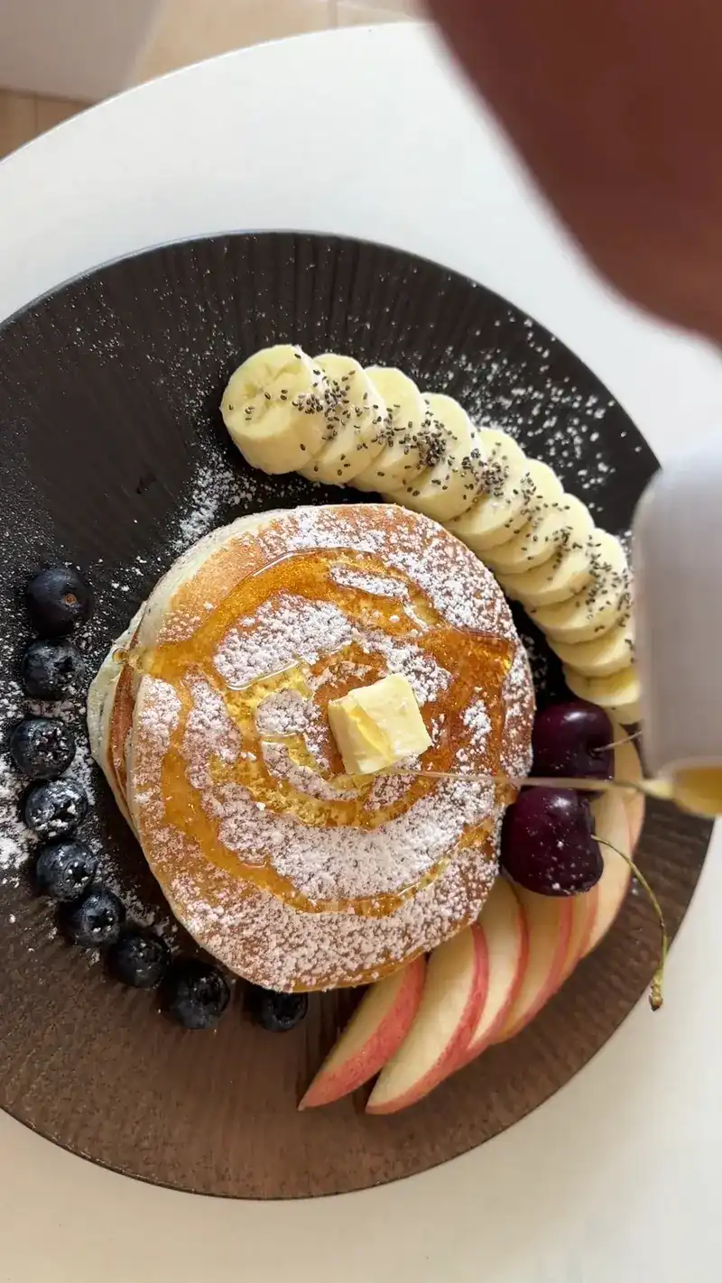 A pancake with butter, banana, berries and apple slices
