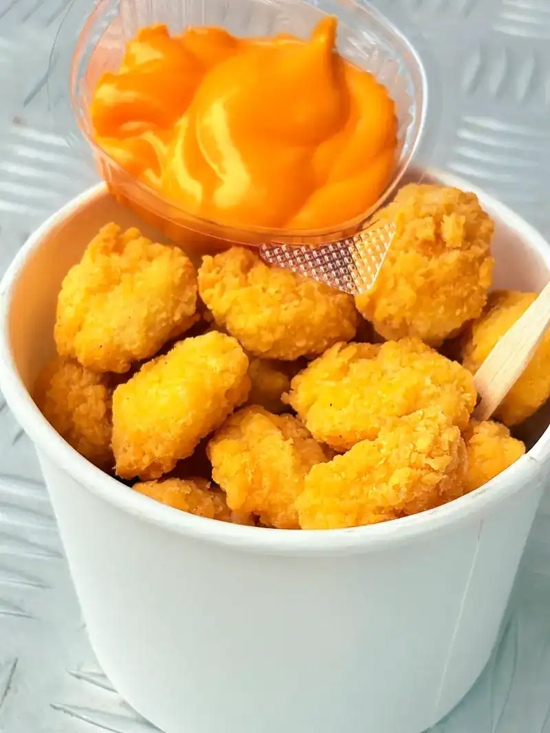 Fried chicken bites in a paper cup with an orange dip, on the truck's metal counter