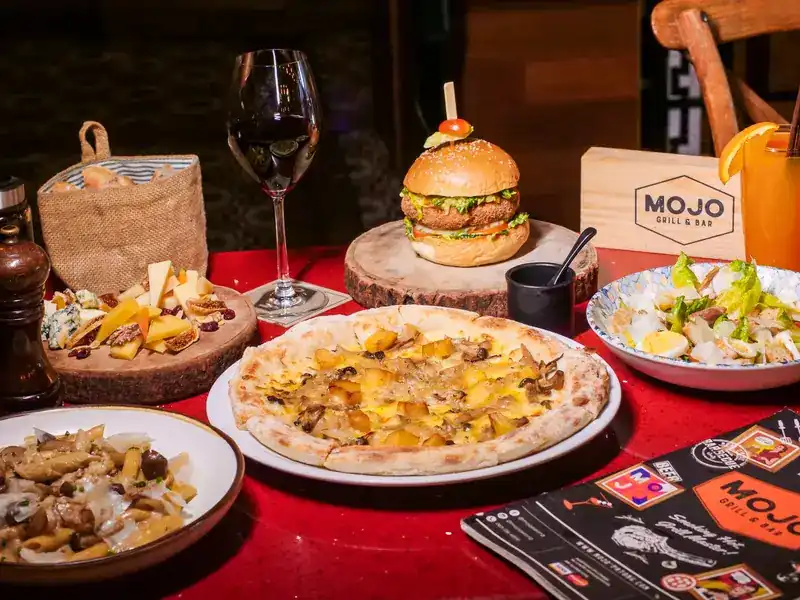 A red table set with a burger, a pizza, pasta, a salad and a cheese board
