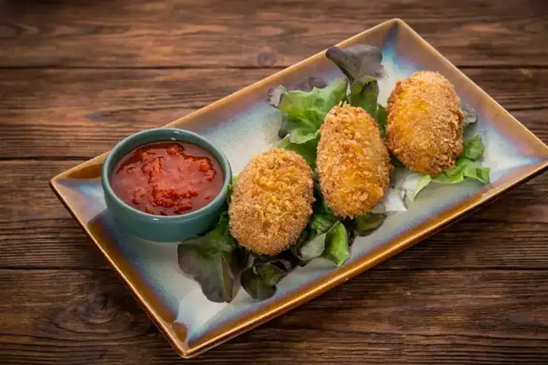 Three potato croquettes with a bowl of tomato sauce