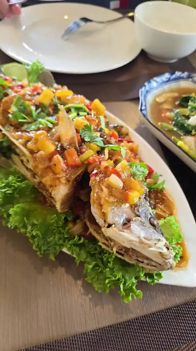 A whole fried fish on lettuce, topped with chopped fruit, chilli and herbs