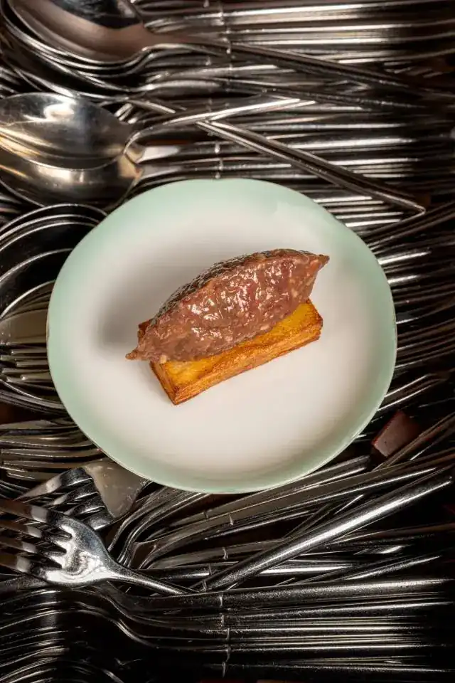 Beef tartare on a potato millefeuille, plate resting on silver cutlery
