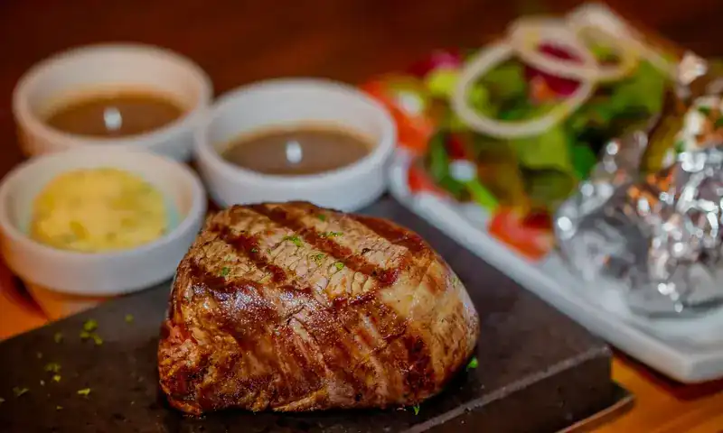 Grilled steak on a hot stone with sauces, salad and a baked potato