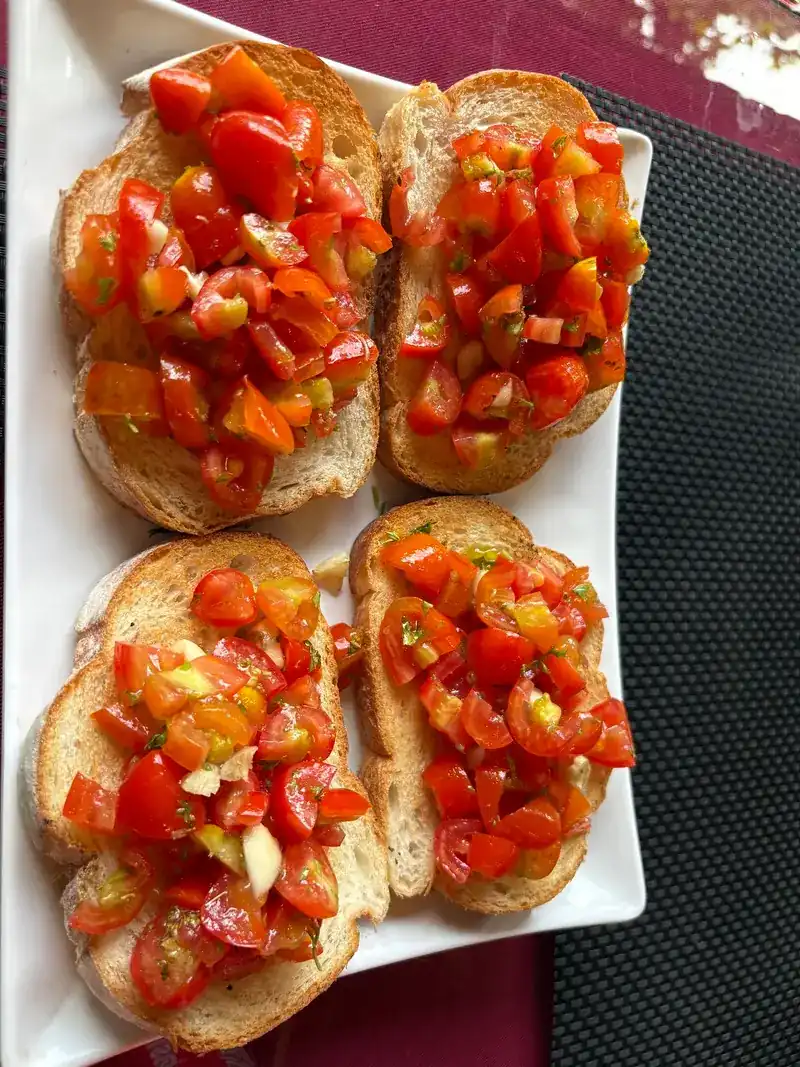 Four slices of toasted bread topped with chopped tomato on a white plate