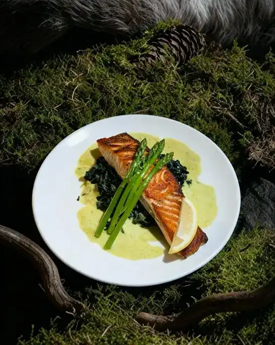 Seared salmon with asparagus and a lemon wedge on a white plate, set on moss