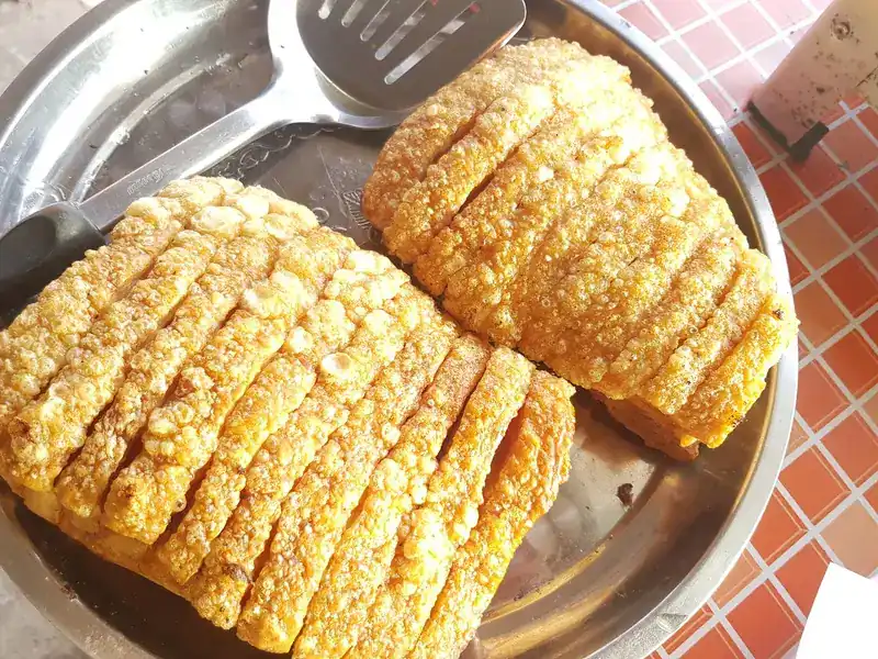 Two slabs of crispy pork belly on a steel tray on the red-tiled counter
