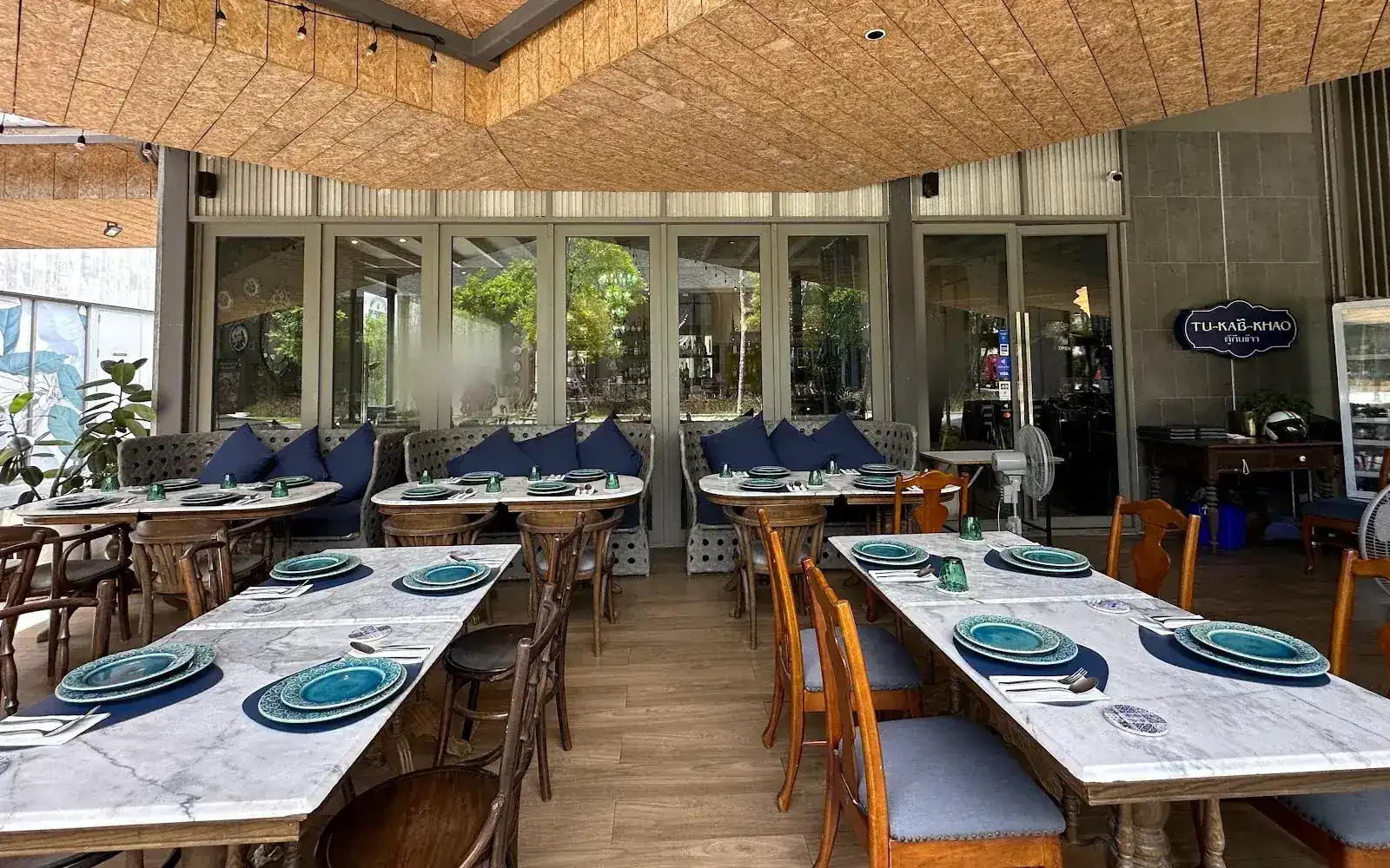 The covered terrace: marble tables set with turquoise plates, navy cushions and the Tu-Kab-Khao sign on the wall