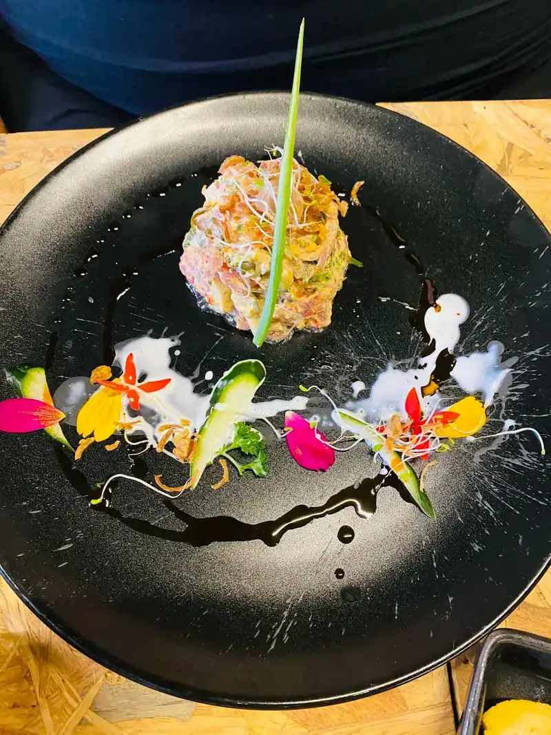 A fish tartare on a black plate, decorated with flowers and sauce