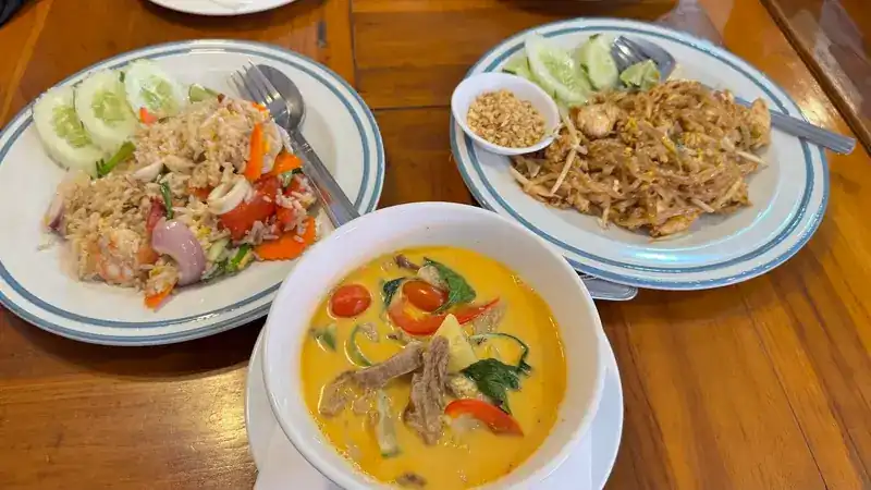 Fried rice, pad thai and a coconut curry on a wooden table / ข้าวผัด ผัดไทย และแกงกะทิบนโต๊ะไม้