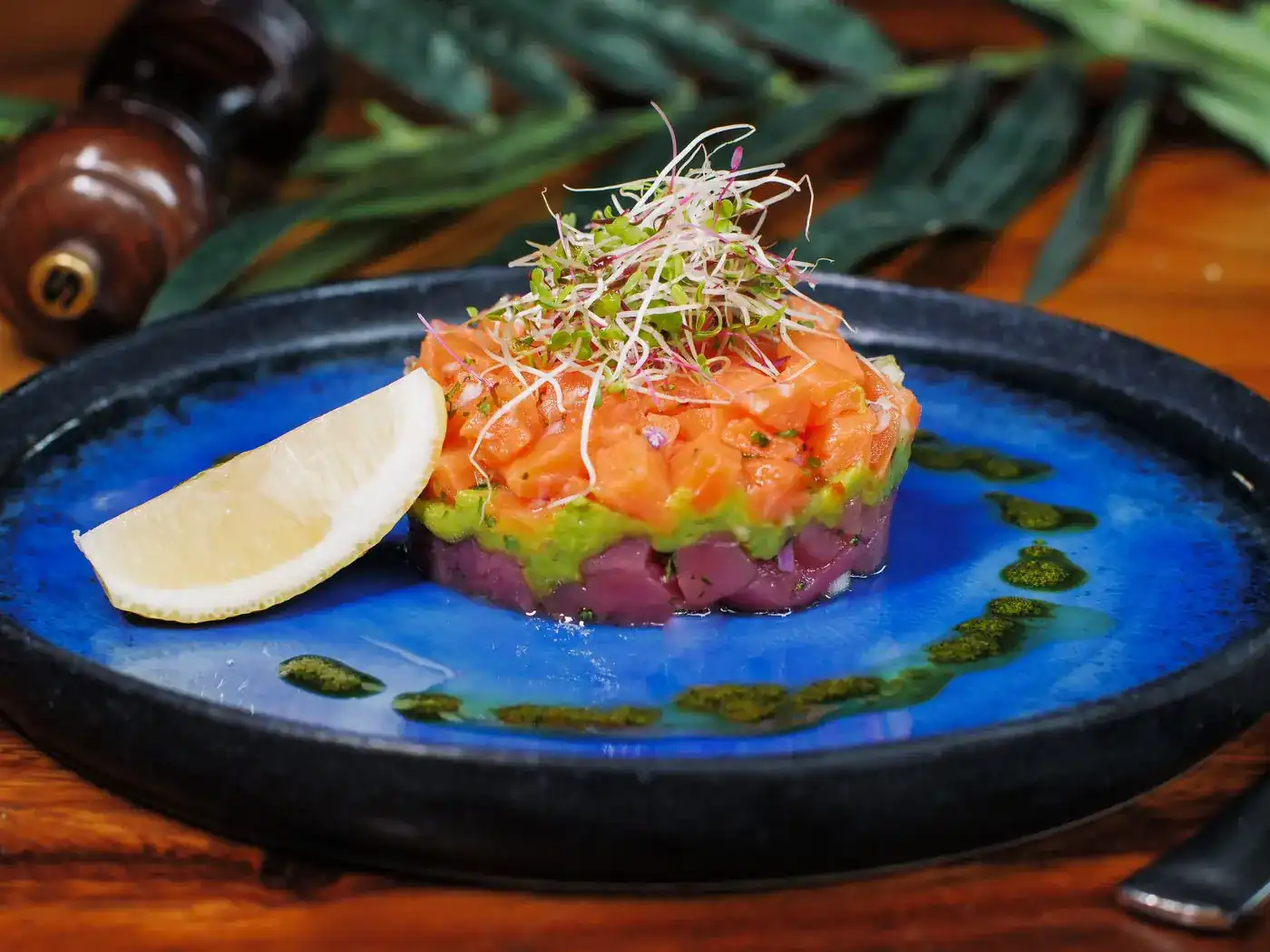 Tuna and salmon layered with avocado on a cobalt blue plate, with a wedge of lemon