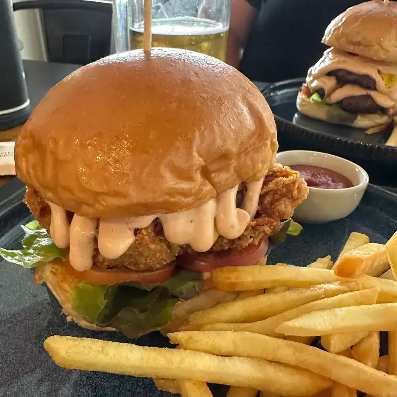 Crispy chicken burger with pink sauce, tomato and lettuce, french fries and a dip on the side