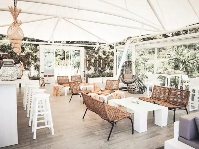 The bar floor under its white awning: woven benches, white tables and stools, a hanging chair