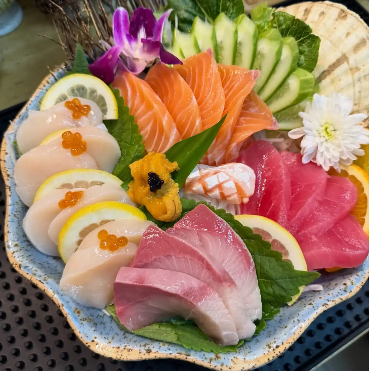 A sashimi platter of salmon, tuna, scallops with salmon roe and sea urchin, garnished with an orchid
