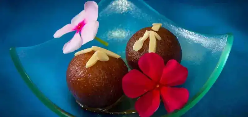 Two Indian sweets topped with almond slivers on a glass dish