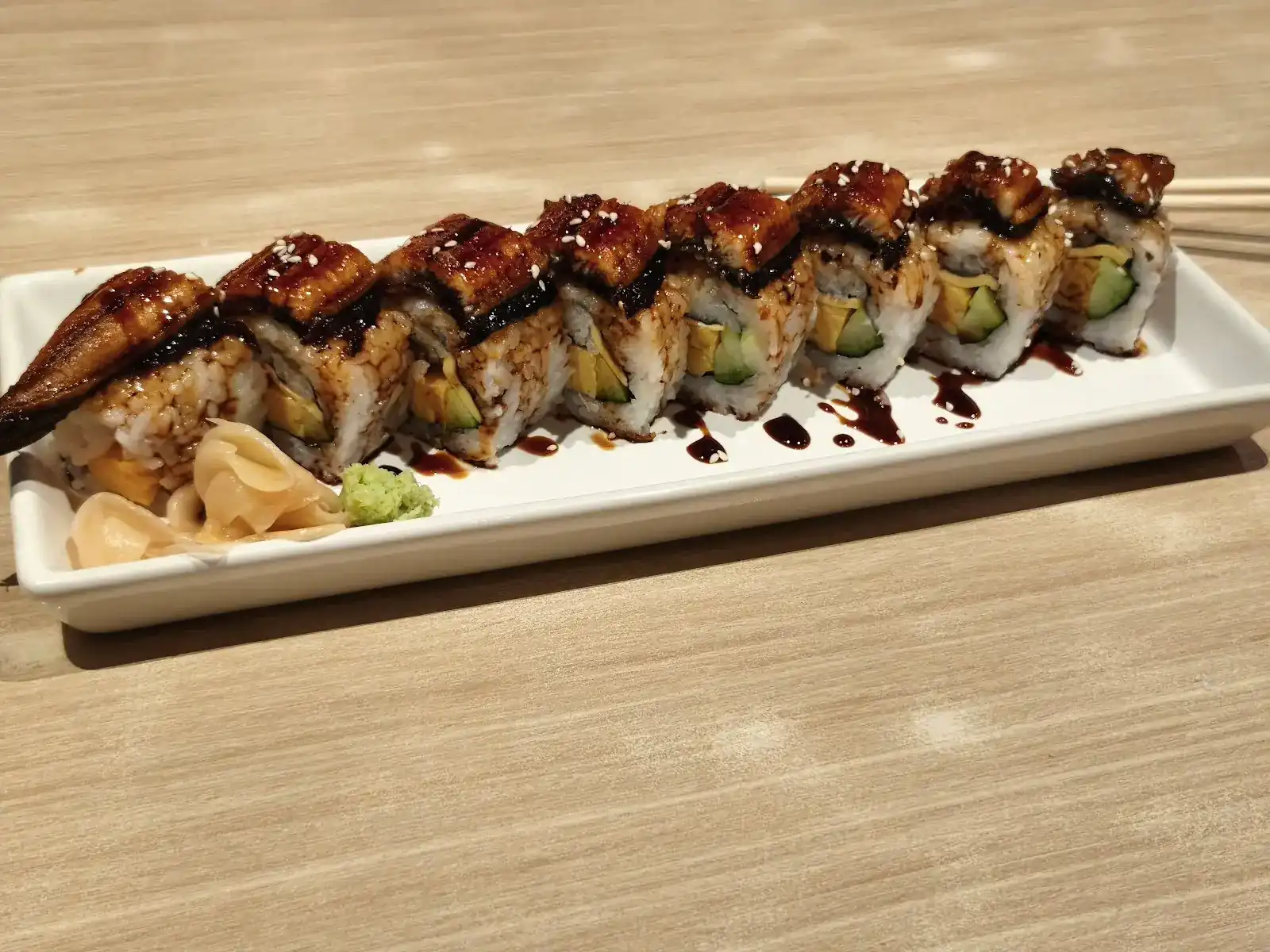Eel-topped maki roll on a white plate with pickled ginger and wasabi