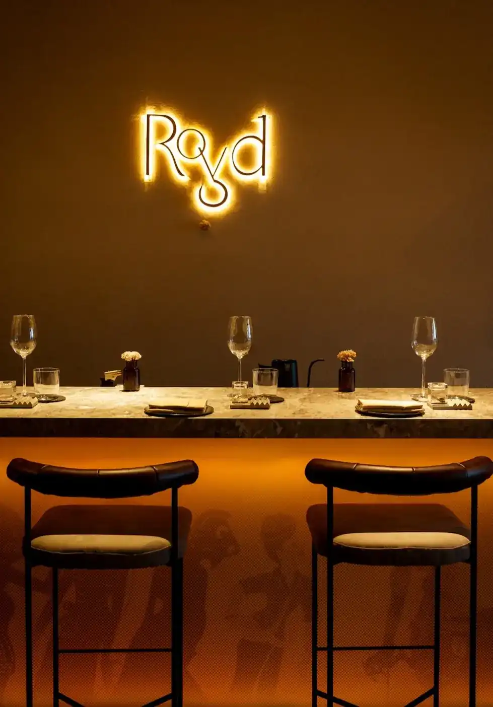 The counter at Royd, set with wine glasses under the restaurant's glowing sign