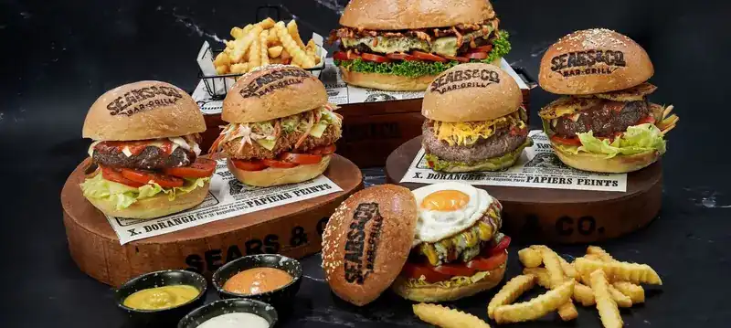 Six burgers on wooden boards with fries and dipping sauces