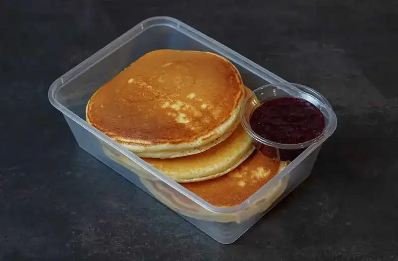 A stack of protein pancakes with a small pot of berry sauce