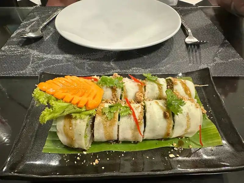 Fresh rolls with sauce and crushed peanuts on banana leaf, with a carved carrot