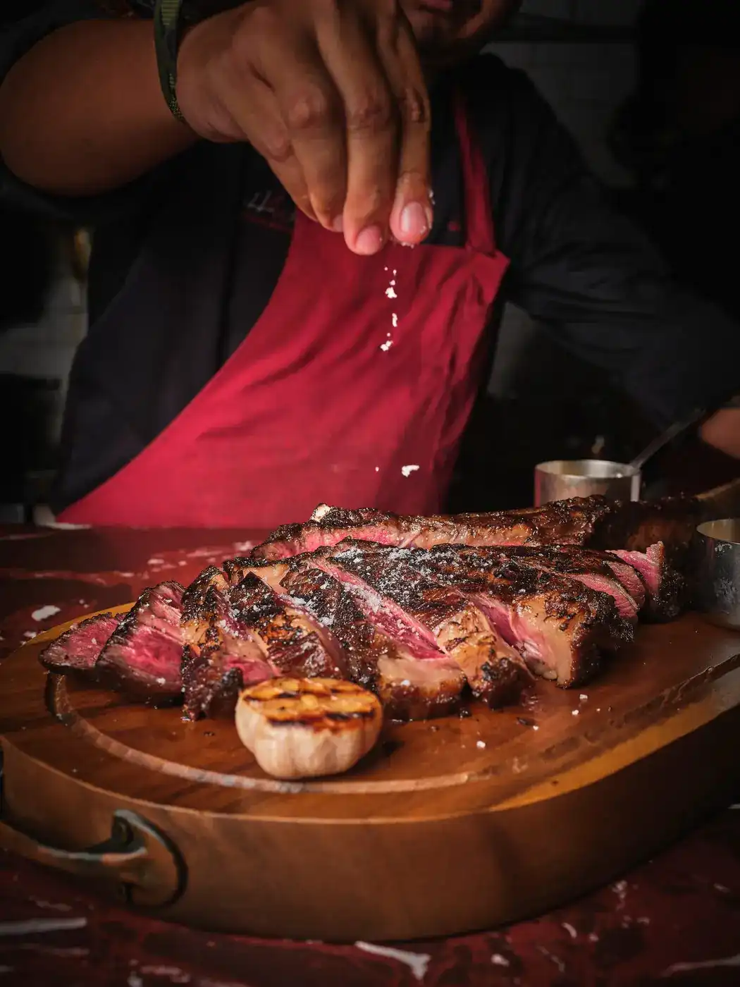 Salt falling from a cook's hand onto sliced grilled steak on a wooden board