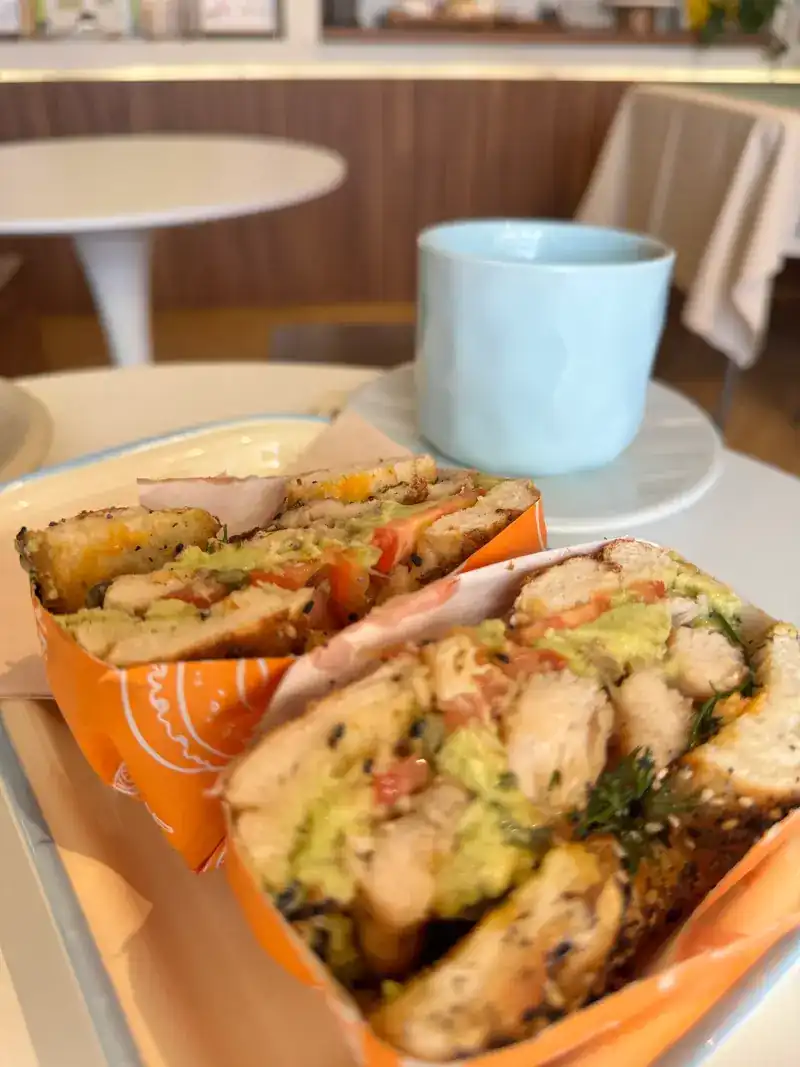 A bagel sandwich with grilled chicken, avocado and tomato, wrapped in orange paper